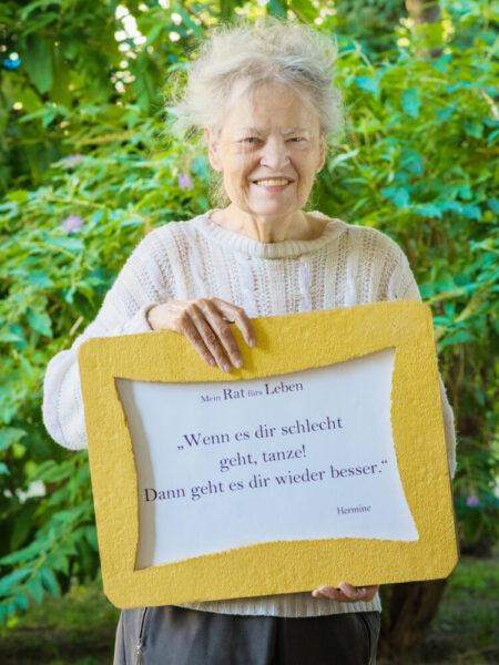 Bewohnerin Hermine der Pflege Simmering mit Schild in der Hand.